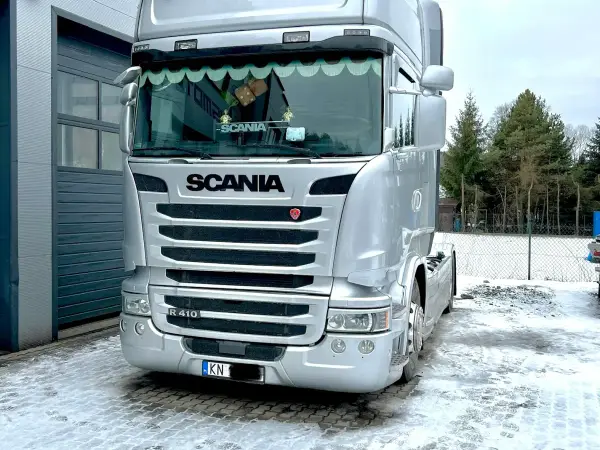 Srebrna Scania R z reflektorami dachowymi na zaśnieżonym placu przed warsztatem