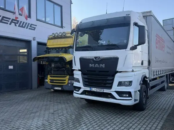 Biały MAN TGX z naczepą kurtynową przed halą serwisową, w tle żółta Scania
