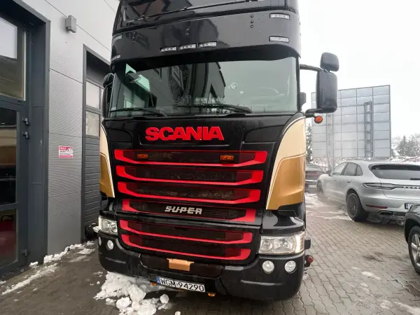 Czarno-złota Scania Super z reflektorami dachowymi przed halą serwisową