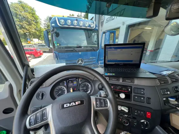 Kabina samochodu ciężarowego DAF z podłączonym komputerem diagnostycznym, w tle Mercedes Actros