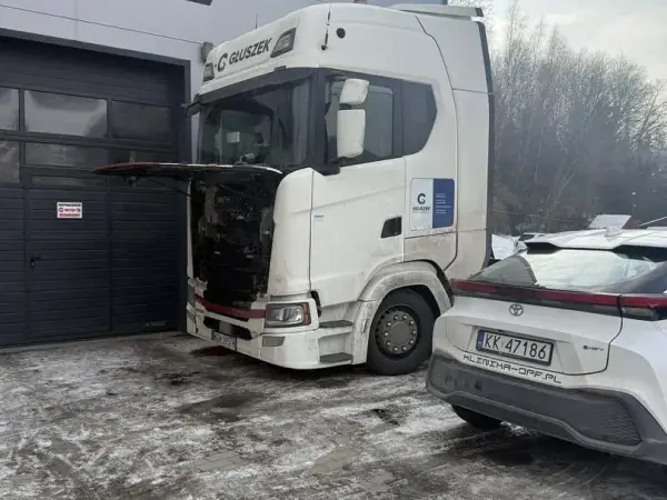 Scania z podniesioną kabiną zimą przed warsztatem, obok samochód osobowy z oznaczeniem Klinika-DPF