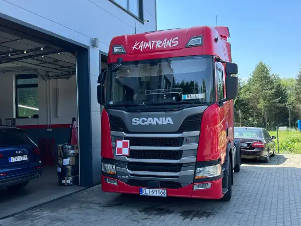 Czerwona Scania firmy Kaimtrans przy otwartej bramie warsztatu