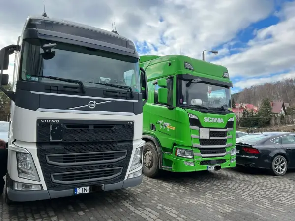 Białe Volvo FH i zielona Scania R450 ustawione obok siebie przed halą serwisową