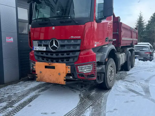 Czerwona wywrotka Mercedes-Benz Arocs z pługiem na zaśnieżonym placu serwisu