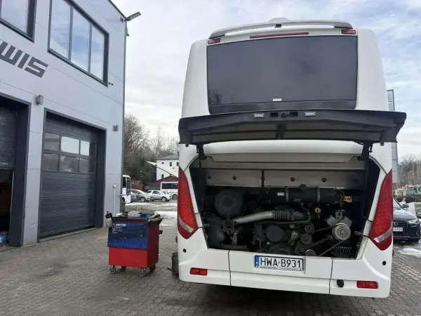Autokar z otwartą klapą silnika i wózkiem narzędziowym podczas obsługi układu wydechowego